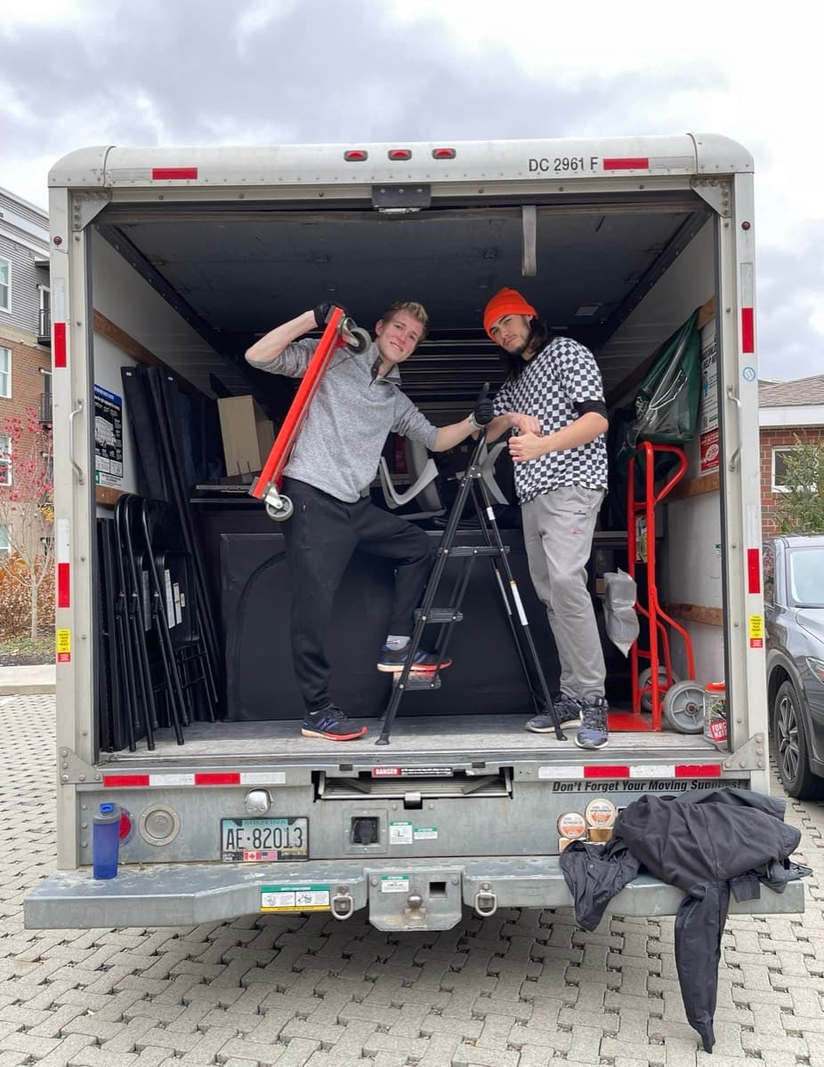 Two DAW movers loading furniture and equipment into the back of a box truck.